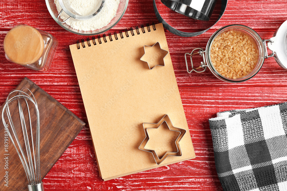 Kitchen utensils with ingredients for pastries and notebook on color wooden background