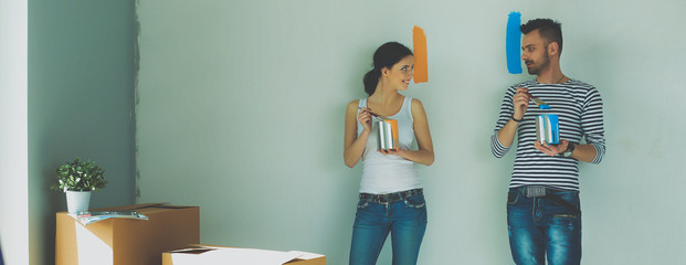 Wall Mural - Portrait happy smiling young couple painting interior wall of new house