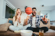 © Mediteraneo - Couple is watching basketball game on the sofa at home.