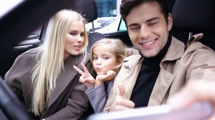 Wall Mural - Happy handsome man making selfie on smartphone while sitting in car with his daughter and wif