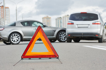 Accident or crash with two automobile. Road warning triangle sign in focus