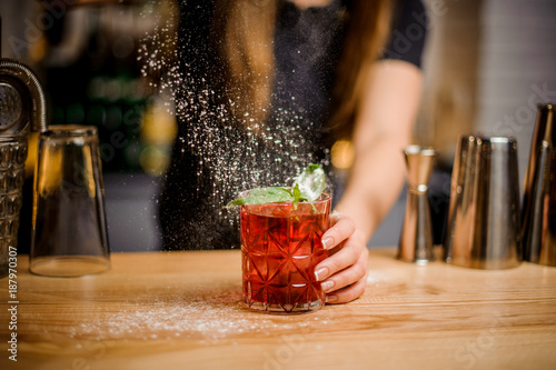 Fotografia, Obraz blondy barmaid finishes preparation of cocktail by adding a bitter of powdered s