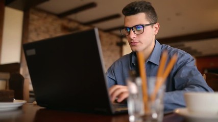 Handsome freelancer businessman in glasses diligently working on laptop in cafe. Man typing on keyboard and searches new job on internet at coffeeshop. Business concept