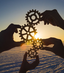 Wall Mural - Four hands collect the gear from the gears of the details of the puzzles. against the background of sunlight. Concept business idea. Teamwork