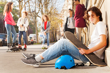 Wall Mural - Boy with skateboard and helmet sitting on sidewalk