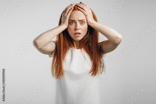 Fotografía emotional redhead girl on white background with fear, open mouth and hands on he