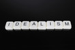 Idealism text word title caption label cover backdrop background. Alphabet letter toy blocks on black reflective background. White alphabetical letters. White educational toy block with words on