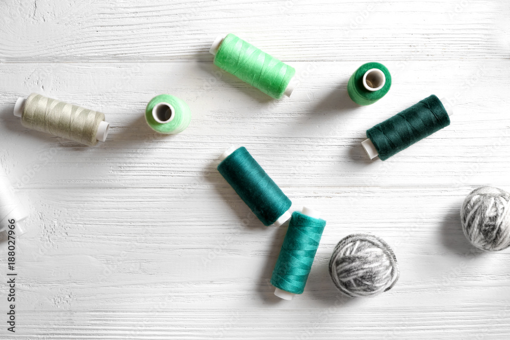 Sewing and woolen threads on wooden background, top view