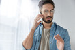 © wayhome.studio  - Portrait of serious bearded male wears glasses and fashionable denim shirt, has phone conversation, gestures with hand as tries to explain something, solves problems via smart phone on distance