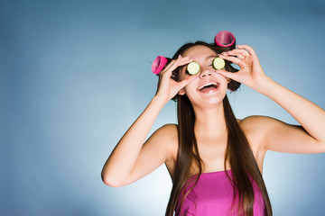 Poster - laughing young girl holding pieces of cucumber for moisturizing the skin on her face, on the head of curlers