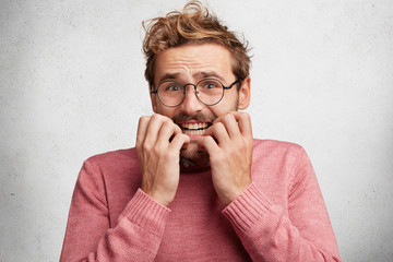 Wall Mural - Worried scared male looks nervously, bites nails, has stressful and frightened expression, going hear results of project work, being not confident in good appriciation. Waiting for something important