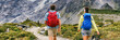 Hikers hiking with camping backpacks walking from behind with bags on outdoor trek in summer nature. New Zealand travel tramping couple on Hooker Valley Track in New Zealand mountains banner.