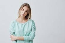 Portrait Of Young Tender Blonde European Woman With Healthy Skin Wearing Light Blue Long-sleeved Looking At Camera With Calm Or Pleasant Expression. Caucasian Female Model Posing Indoors