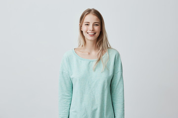 Wall Mural - Horizontal portrait of pleasant-looking Caucasian female with long blonde hair, wearing white casual blue sweater, looking happily at camera. Beauty and youth