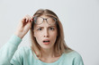 © Cookie Studio - Surprised young female model with long blonde hair, wears glasses and blue long-sleeved shirt, looks with terror at camera as notices something unexpected, hears bad news, isolated against gray wall