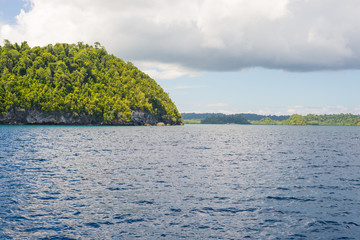 Wall Mural - Rocky coastline of island spotted by islets and covered by dense lush green jungle in the colorful sea of the remote Togean Islands (or Togian Islands), Central Sulawesi, Indonesia.