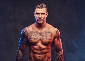 Wall Mural - A muscular tattooed man on a dark background.