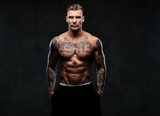 Wall Mural - A muscular tattooed man on a dark background.