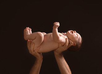 Poster - Hands of father holding cute little baby on dark background