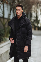 Stylish man wolk on the street. Winter cold outfit. Big jacket with white sneakers. Blured background street. Profecional model photo.