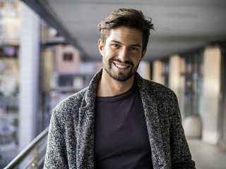 one handsome young man in urban setting in european city, standing and smiling to camera happy