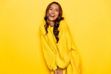 funny young woman with curly hair in yellow sweater, widely smiling,. isolated on yellow background.