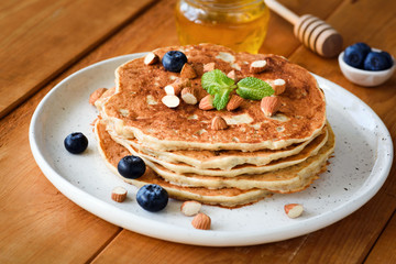 Wall Mural - Gluten free pancakes with almonds and blueberries on white plate on wooden table