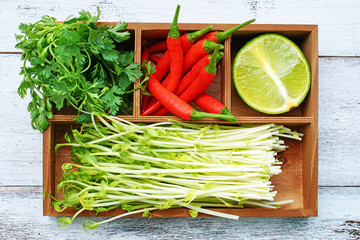 Closeup of chili pepper, lime, parsley and sprouts in rustic wooden box. Eastern cooking ingredients.