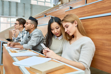 international group of students sitting in row at desks in modern lecture hall waiting for class in 