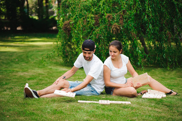 Wall Mural - Young man and woman playing giant dominoes in the Park on the grass.