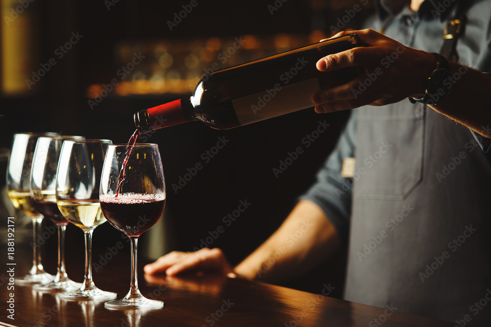 Bartender pours red wine in glasses on wooden bar counter - obrazy, fototapety, plakaty 