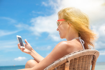 Young beautiful woman with mobile phone on the shore of the tropical sea in a cafe. Communication and internet in travel concept