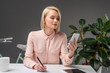 © LIGHTFIELD STUDIOS - portrait of young businesswoman using smartphone at workplace isolated on grey