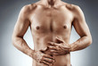 © Romario Ien - Man holding his stomach in pain. Photo of man with naked torso experience irritable bowel syndrome on grey background. Medical concept