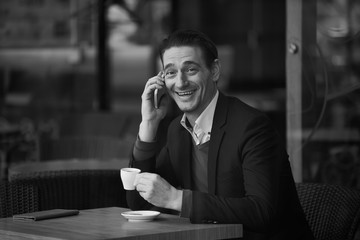 Aufkleber - Portrait of happy male speaking by phone while sitting at table in cafe. Black and white photo. Relax and communication concept