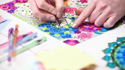 Wall Mural - Color video of a young unrecognisable woman colouring in an adult colouring book. New art therapy and stress management trend. Close up shot, hand detail.