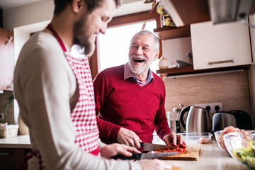 Hipster son with his senior father cooking in the kitchen.