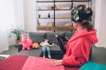 Wall Mural - mother and baby together engaged in housework Ironing clothes . Housewife and kid doing homework. Woman with little child in the living room. Homemaker doing many tasks while looks after her infant