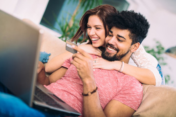 Happy interracial couple shopping online at home, using credit card, laughing