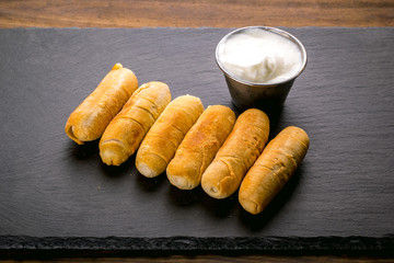 Tequeños, Typical Venezuelan snack with garlic sauce on a black stone background.