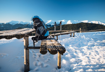 Hiking backpack and trekking poles infront of a mountain range in winter. Clear blue sky over the mountain range.