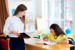 © yolya_ilyasova - Young woman teacher helps the female student to understand a lesson. Student sits at her desk with a large book in the classroom and listening to teacher.