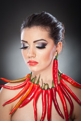 Beautiful young woman portrait with red hot and spicy peppers, fashion model with creative food vegetable make up looking side to empty copy space, isolated over black background. Red chili Paprika.