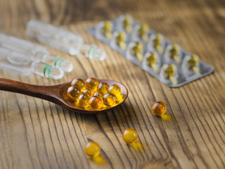 Wall Mural - Pills of fish oil a wooden spoon with vials and blister in the background. Traditional medicine.