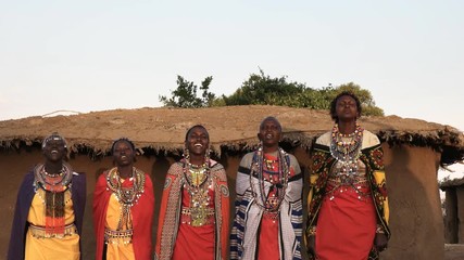wide shot of five maasai women in traditional dress singing and dancing in a village near maasai mar