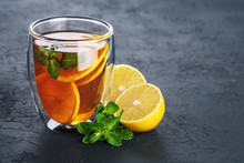 Hot tea with mint and lemon in a glass with double walls on a dark background.