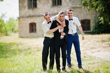 Groom posing with two groomsmen on a sunny wedding day next to the castle.