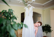 Pretty bride stands before a wedding dress wich hangs on the chandelier