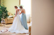 Bridesmaid in blue dress helps pretty bride to put on a wedding dress