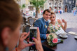 Woman takes a picture of stunning newlyweds sitting in the cafe